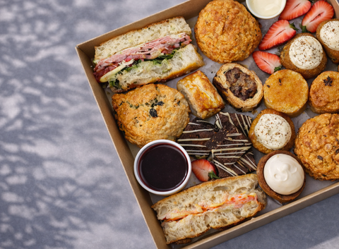 Assorted food items including sandwiches, pastries, and cookies in an afternoon tea box on a textured surface.