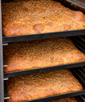 Loaves of focaccia bread with sesame seeds on a baking rack.