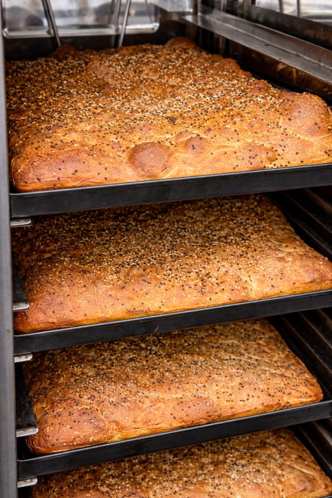 Loaves of focaccia bread with sesame seeds on a baking rack.