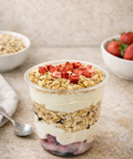 Yogurt with granola and strawberries in a glass container on a stone surface.