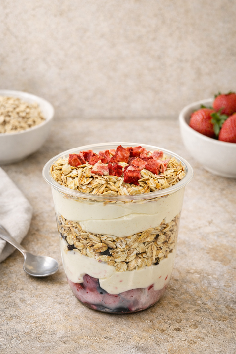 Yogurt with granola and strawberries in a glass container on a stone surface.